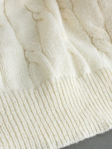 Detailed close-up of cream white cable knit sweater fabric with ribbed cuffs texture