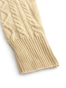 Detailed view of cable knit pattern and ribbed cuff on a beige knitted dress sleeve