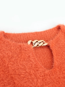 Detail of bright orange fuzzy knit sweater featuring a stylish gold chain at the neckline