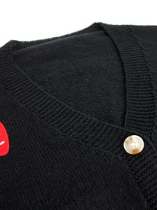 Detail of V-neck knitted cardigan with black wool texture and red heart embroidery