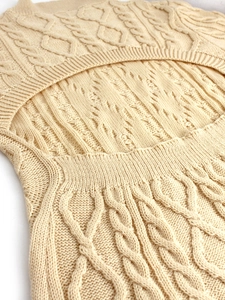 Detail of beige cable-knit dress featuring textured patterns and open back cut-out design