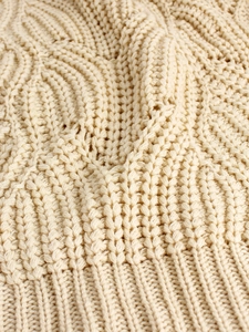 Close-up of beige chunky knit sweater featuring cable patterns and ribbed cuffs