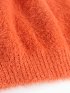 Close-up of orange plush knit fabric with ribbed cuffs on an off-shoulder sweater