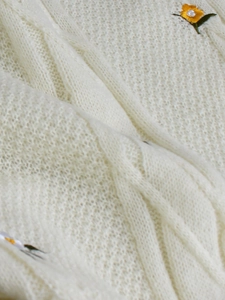 Close-up of cream cable knit fabric with delicate yellow floral embroidery and green leaves
