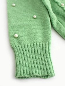 Close-up of light green knit sleeve with ribbed cuffs and scattered pearl accents