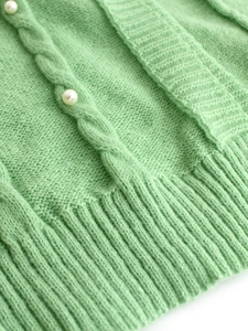 Close-up of cable knit cardigan with pearl embellishments in soft mint green texture