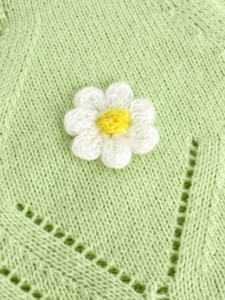 Detail of light green knit fabric featuring hollow wave patterns and 3D crochet daisy