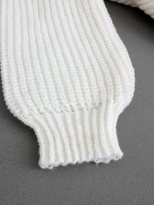 Nahaufnahme der cremefarbenen Rippbündchen und der detaillierten Textur des Strickpullovers