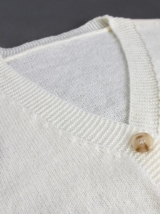 Close-up of V-neck knitted cardigan with marble texture button on off-white fabric