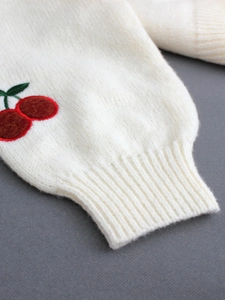 White knit cardigan with detailed cherry embroidery and ribbed cuffs on dark background