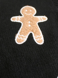 Macro detail of gingerbread man patch on black knit sweater showing the fabric texture
