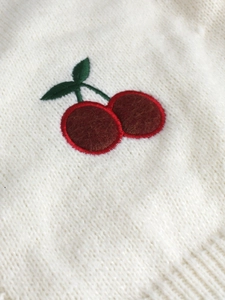 Detail of 3D cherry embroidery on beige knit sweater with red velvet texture and green leaves