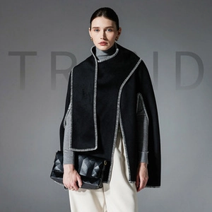 Detail of black poncho shawl with white contrast stitching and geometric texture handbag