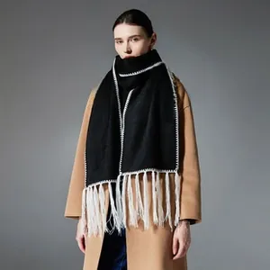 Close-up of black wool scarf featuring white piped edges and long fringe tassels
