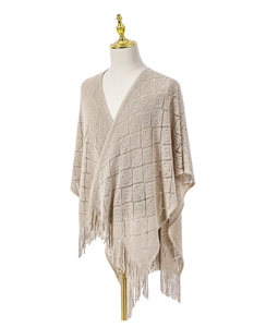 Détail d'un châle en maille beige ajourée avec motifs géométriques et longues franges