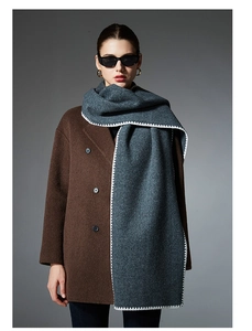 Detail of dark grey wool scarf with white wavy scalloped edges on a brown wool coat