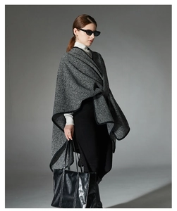 Detail of grey striped knit shawl wrap with black fabric trim and draped silhouette