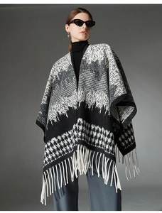 Detail of wool poncho featuring black and white houndstooth patterns and fringe hem