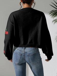 Detail of red cherry embroidery on black knit cardigan with close-up stitch texture