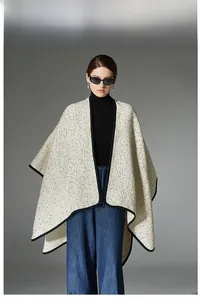 Detail of cream white tweed poncho with black trim over casual jeans and turtleneck