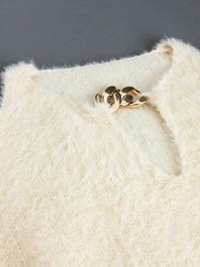 Close-up of fluffy off-white sweater featuring V-neckline with chunky gold chain detail