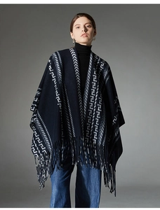 Detail of navy blue knit poncho featuring geometric jacquard patterns and soft fringe trim