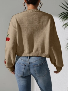 Detailed view of 3D cherry embroidery on the sleeve of a khaki knit sweater