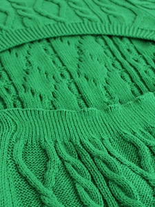 Detailed macro view of emerald green cable knit fabric with hollow patterns and ribbed cuffs