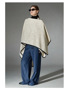 Detail of tweed wool poncho with black ribbon trim and elegant textured fabric