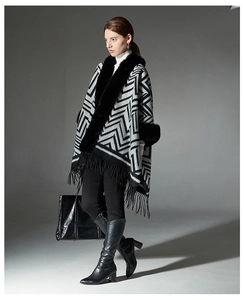 Détail d'un poncho rayé gris avec col en fausse fourrure noire et franges sur un modèle