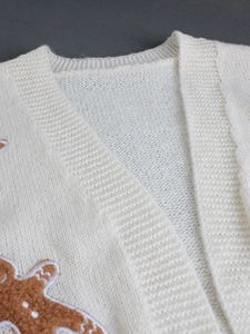 Detailed macro view of cream knitted cardigan featuring cute gingerbread man embroidery