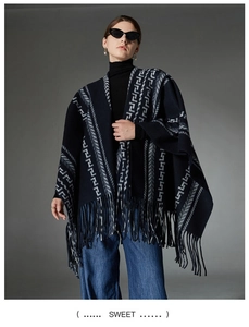 Detail of navy knit poncho featuring white geometric Greek patterns and fringe hem