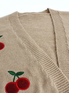 Detail of beige knitted cardigan showing V-neck design and red cherry embroidery texture