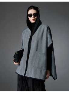 Detail of grey herringbone hooded poncho with black piping and functional side pockets