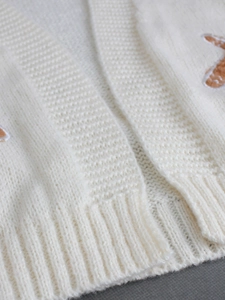 Close-up of cream knit cardigan featuring ribbed hem and detailed gingerbread man embroidery