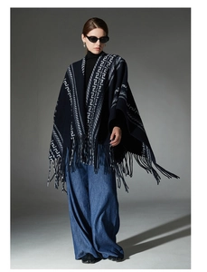Detail of navy blue knit poncho with white geometric patterns and tassel fringe trim