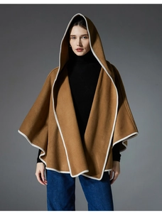 Detail view of caramel hooded wool cape with white piping on a grey background