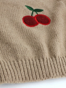 Close-up of oatmeal knit sweater featuring detailed red cherry embroidery and ribbed hem