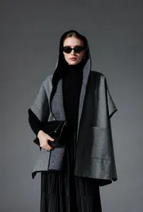 Detail of grey herringbone hooded poncho with black piping and functional side pocket