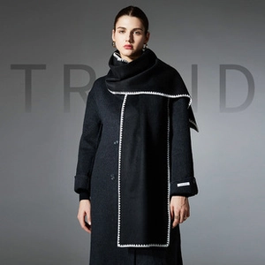Detail view of black woolen scarf with white zig-zag stitching and fashion label