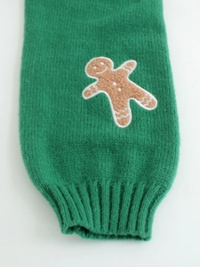 Detailed close-up of green knit sweater cuff with embroidered gingerbread man pattern