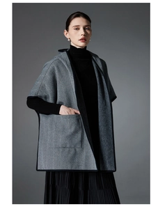Detailed macro view of gray herringbone wool texture and black ribbon edge on a woman poncho