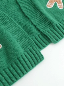 Detail of green knit cardigan featuring gingerbread man patch and ribbed hem texture