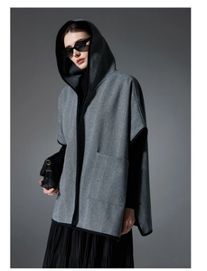 Detail of grey herringbone hooded cloak featuring black piping and large front pockets