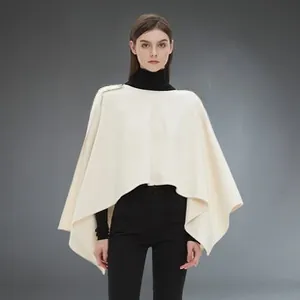 Detailed close-up of cream-white poncho shawl with elegant metal button and soft wool texture