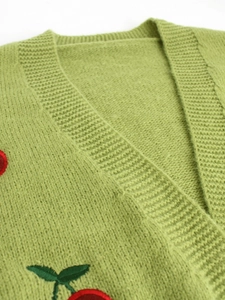 Detailed close-up of cherry embroidery and ribbed V-neckline on green knit cardigan