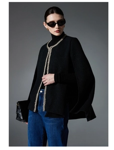 Close-up of black tweed cape jacket with gold-white braided trim detail and rich texture