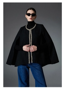 Close-up of elegant black tweed poncho with golden braided trim on stylish female model