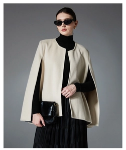 Detailed texture of beige wool sleeveless shawl wrap styled with a black pleated skirt