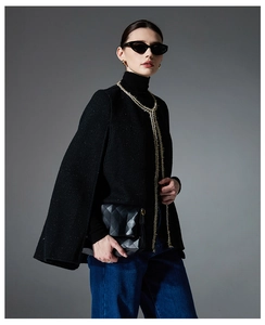 Detailed close-up of a black tweed cape jacket with gold braided trim and elegant texture